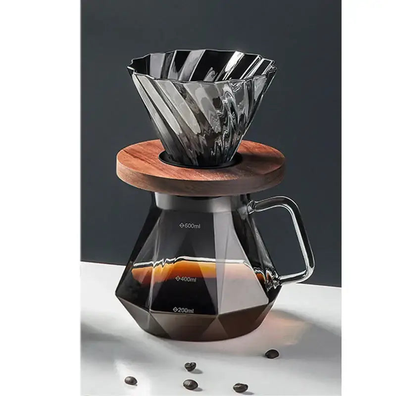 A sleek faceted dark tinted diamond glass coffee carafe with a fluted metallic filter cup on a wooden coaster