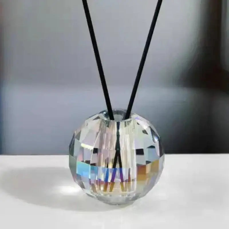 A faceted clear crystal aroma diffuser with black reed sticks on a geometric gold crystal ball base for bedroom decor