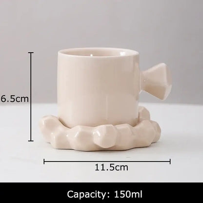 Cream-colored ceramic mug set with faceted handle and matching saucer in elegant minimalist coffee mug design