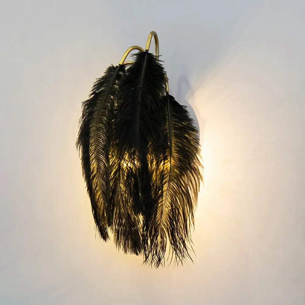 Black ostrich feather wall light fixture with gold-toned metal mounting for bedroom sconce use