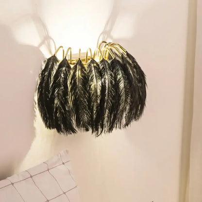 Black feather wall light fixture with gold-toned metal hooks for bedroom use as a stylish wall light sconce