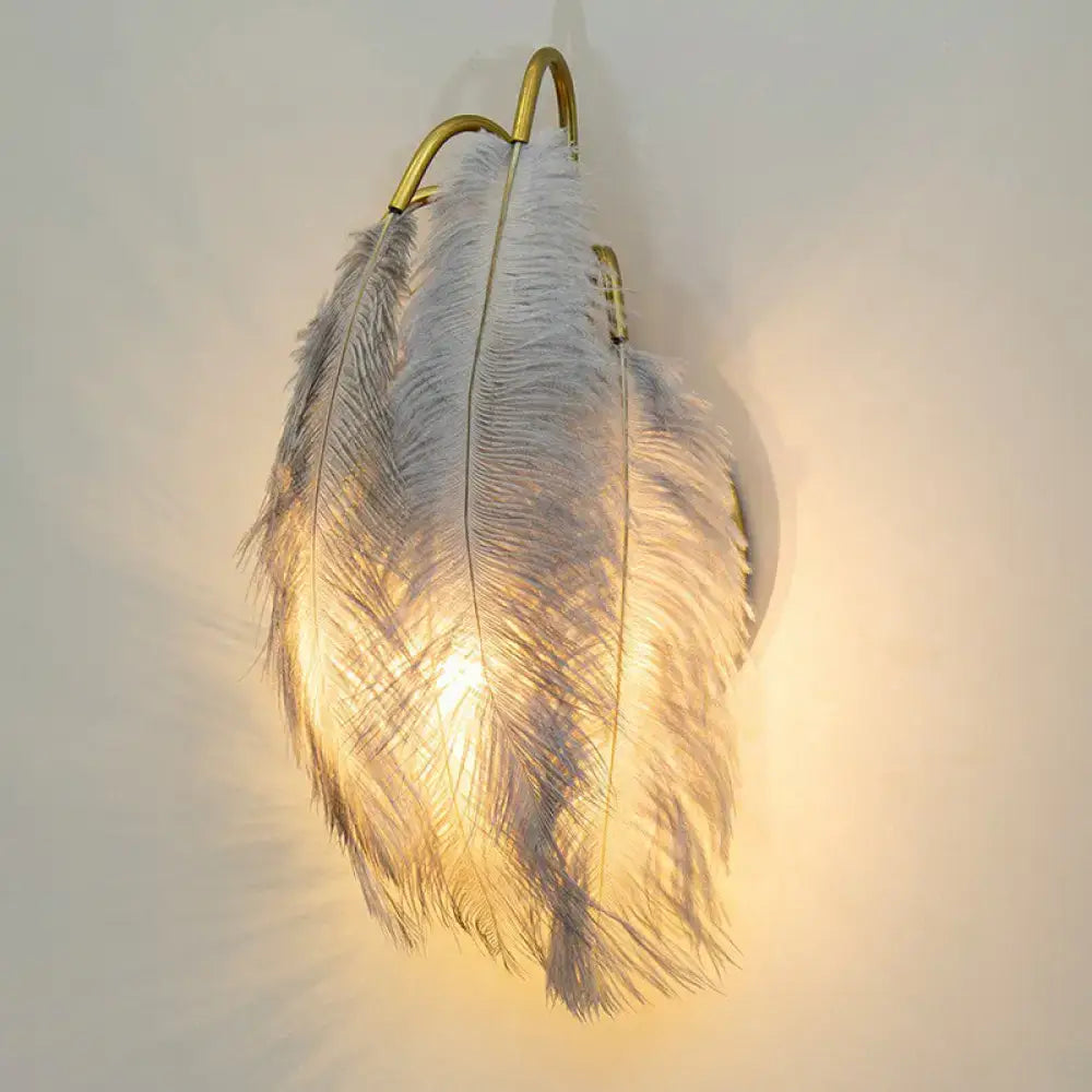 White ostrich feather wall light fixture with gold-toned metal hooks for elegant bedroom wall lighting