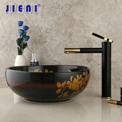 Black ceramic vessel sink with gold floral decals and red stripe paired with swivel brass faucet