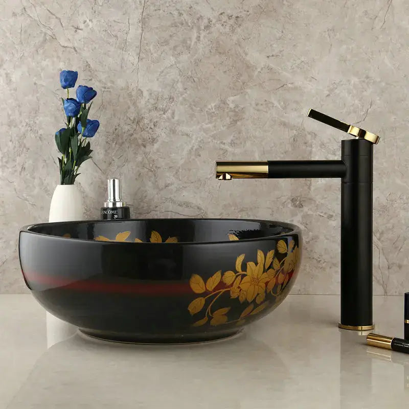 Black ceramic vessel sink with gold floral decals and red accent band paired with swivel brass faucet