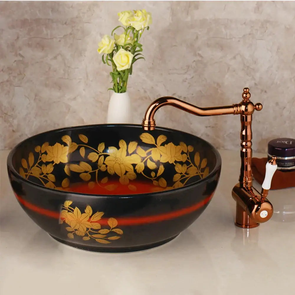 Black ceramic vessel sink with gold floral patterns and red accent stripe paired with swivel brass faucet