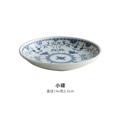 A delicate white ceramic dining set dish with blue floral and vine patterns featuring a central circular motif