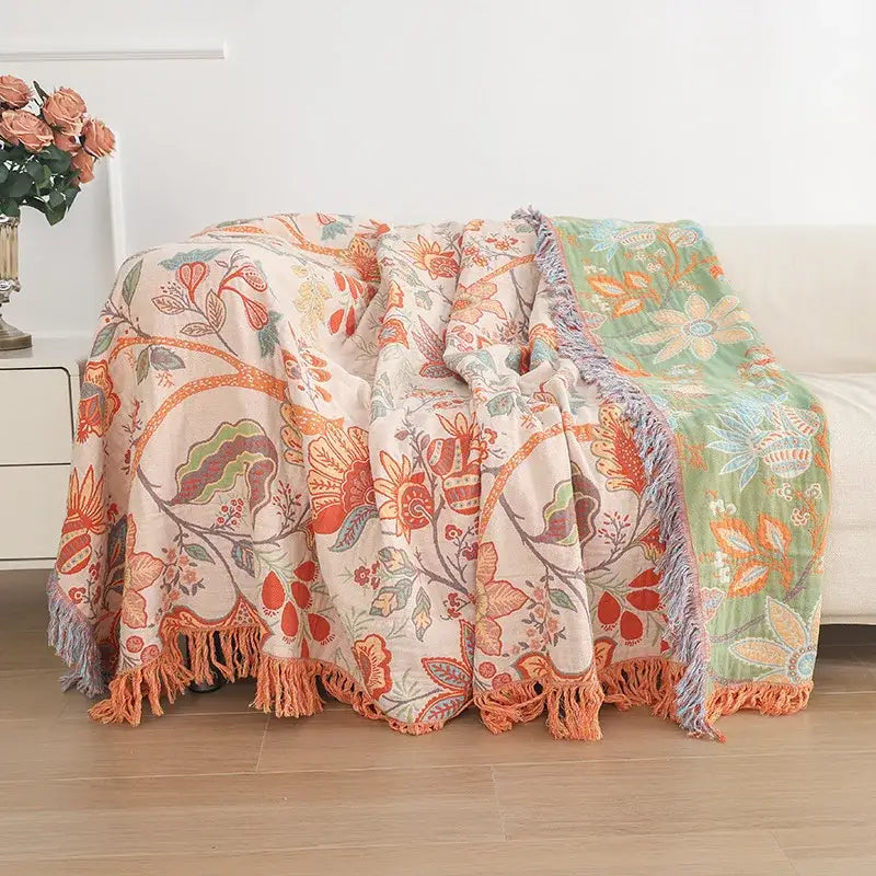 A cozy double cotton bohemian throw blanket with vibrant orange green floral pattern and soft fringed edges on cream