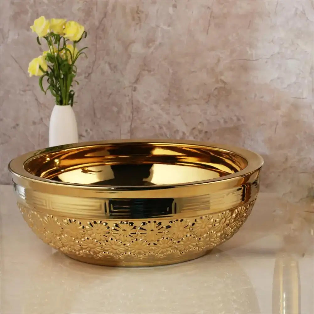 Golden ceramic washbasin with intricate floral embossing and polished interior paired with brass mixer faucet