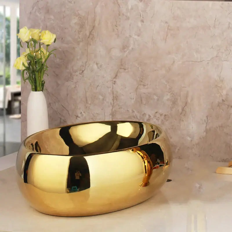 Shiny golden ceramic washbasin with smooth reflective surface and rounded edges paired with brass mixer faucet decorbites