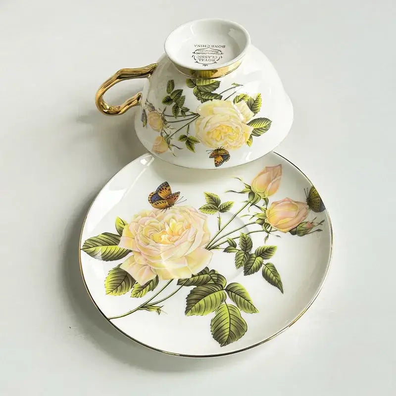 Delicate white porcelain coffee cup and saucer set with gold trim and decorbites flowers pattern featuring yellow roses and butterflies