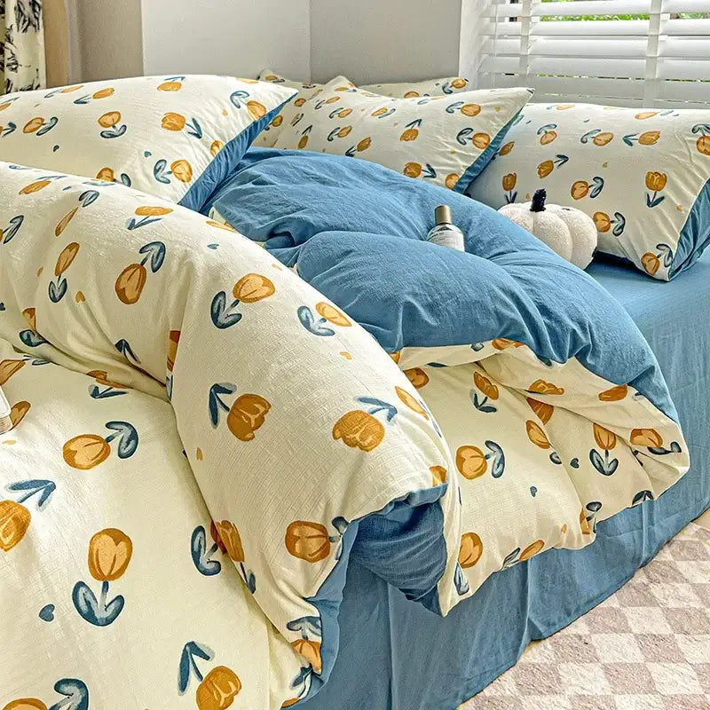 Cream-colored cotton flower printed comforter set with orange tulips and teal stems layered over blue comforter decorbites