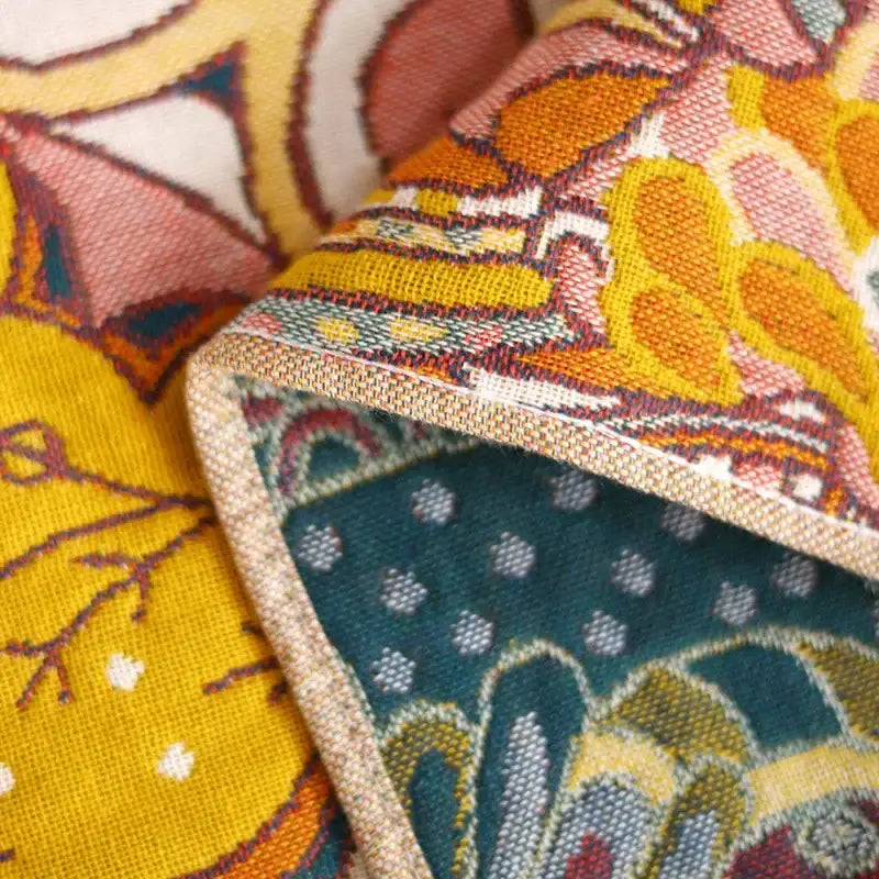 A vibrant cotton gauze bath towel with bold yellow and orange floral patterns and teal dotted backing for bathroom decor