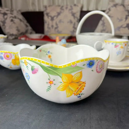 A white porcelain dinnerware set bowl with scalloped rim and vibrant floral patterns including yellow daffodils and pink blossoms