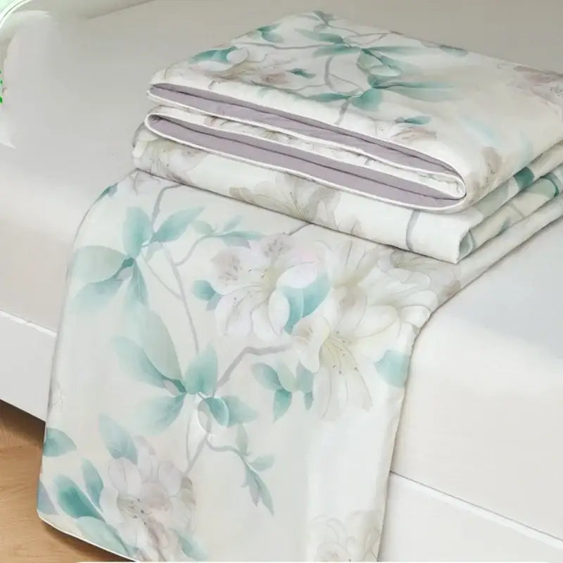 A folded floral teal and white decorbites knitted cotton print summer quilt with subtle gray accents