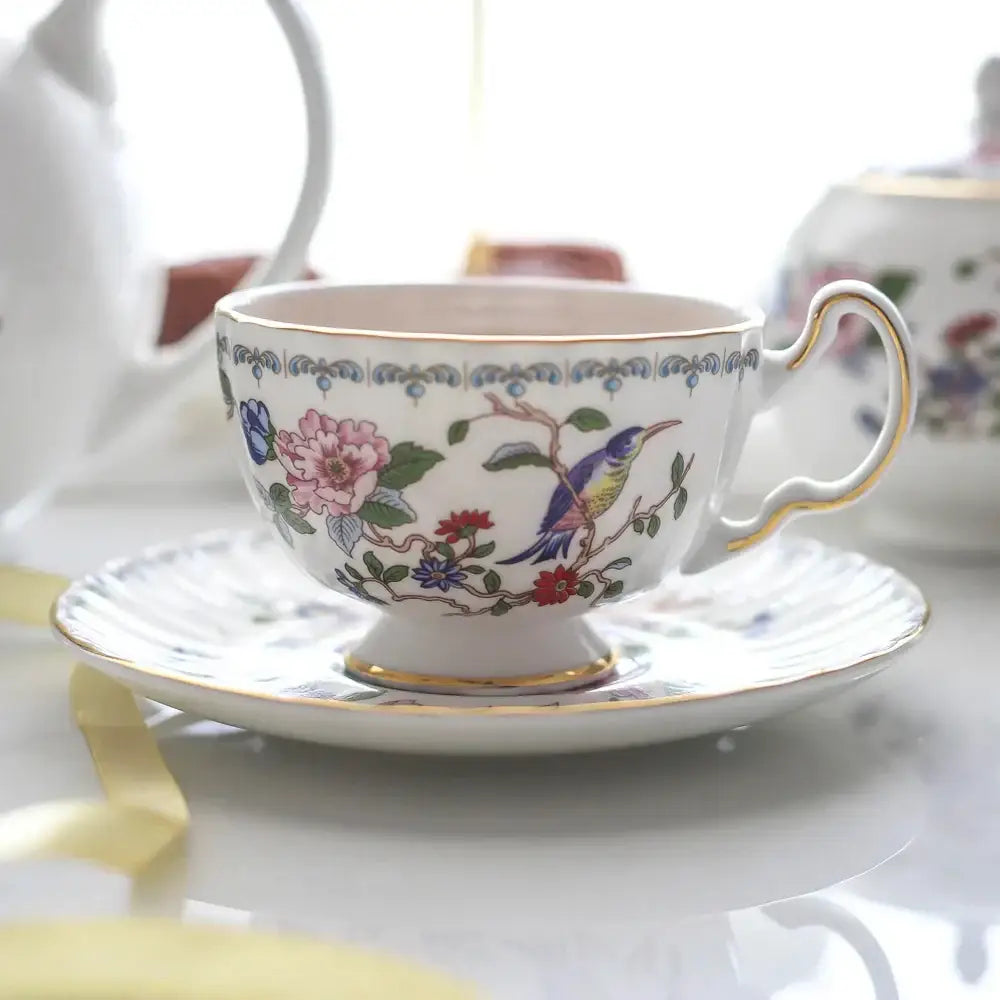 A delicate white bone china tea cup set with gold rim and vibrant floral and bird motif for elegant dining