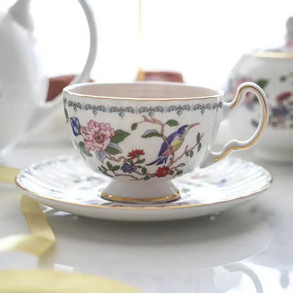 A delicate white bone china tea cup set with gold rim and vibrant floral and bird motif for elegant dining