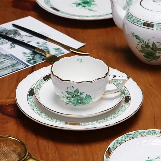 White porcelain tea cup with green floral design and gold trim featuring scalloped rim in tea cup set
