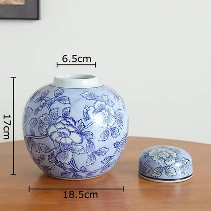 A round light blue ceramic tea caddy with dark blue floral patterns next to a white porcelain vase for living room decor