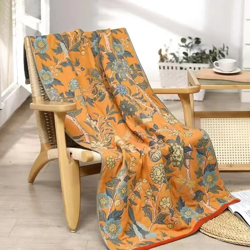 A vibrant orange cotton gauze floral bath towel with blue and green patterns draped over a wooden chair