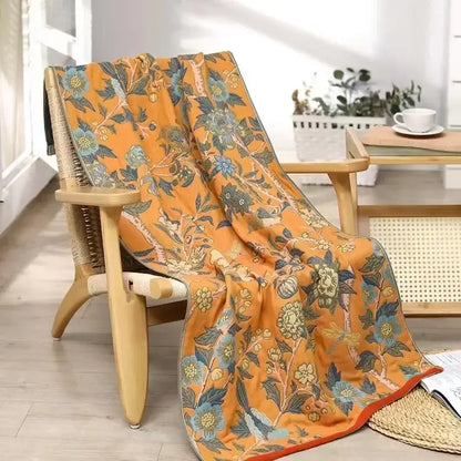 A vibrant orange cotton gauze floral bath towel with blue and green patterns draped over a wooden chair