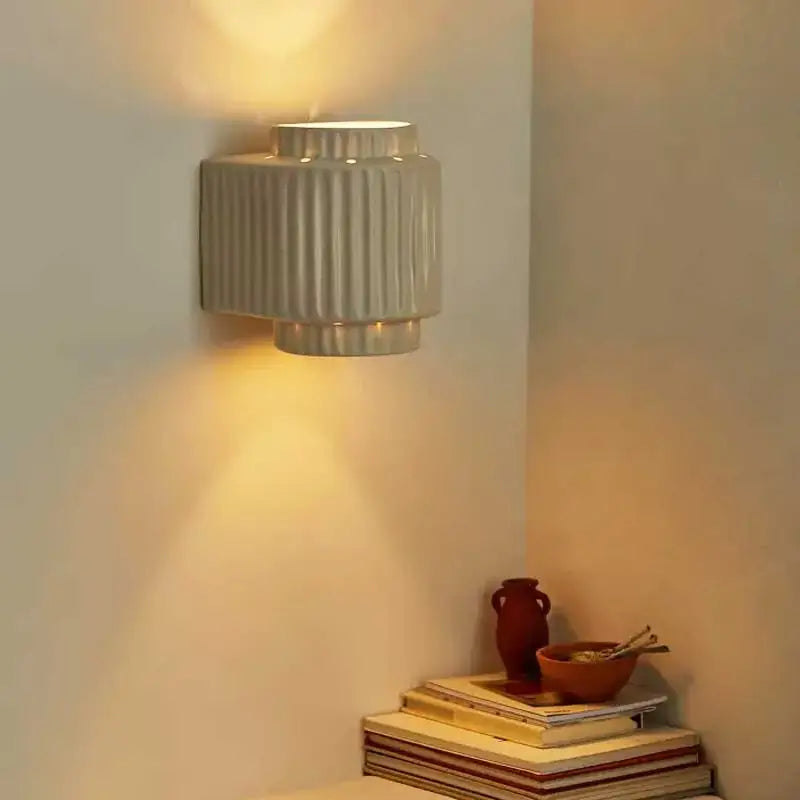 A sleek cream white led ceramic wall lamp with vertical ridges and tiered design for bedroom decor by decorbites