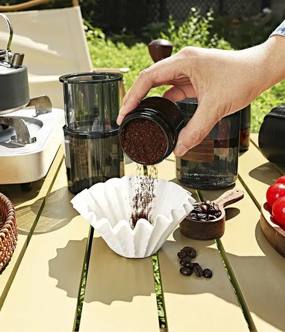 Dark brown coffee grounds poured from black jar into fluted white disposable paper coffee filters decorbites kitchen basket style