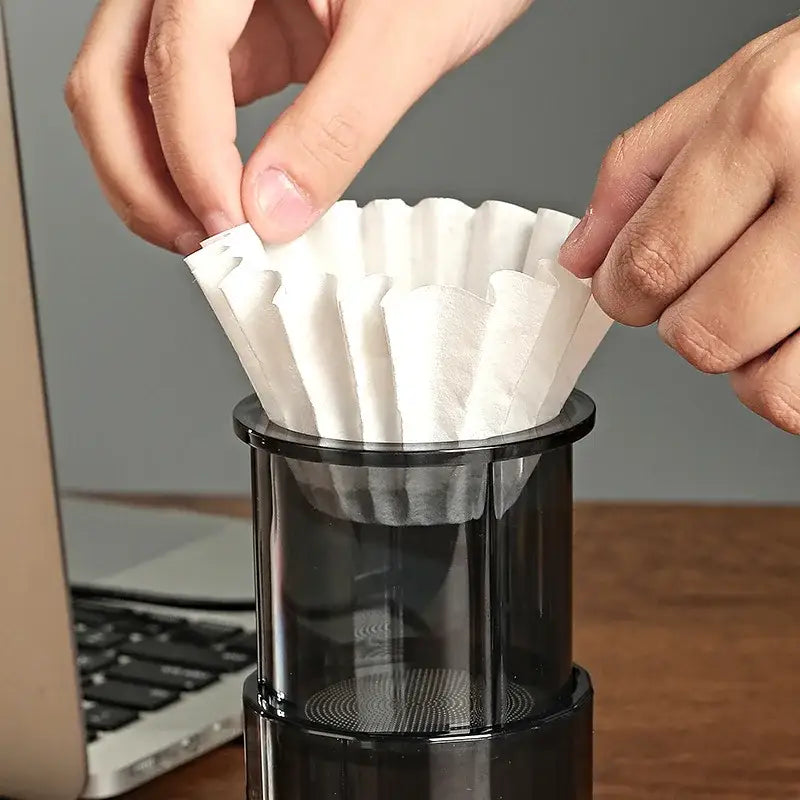 Fluted white disposable paper coffee filters being placed into a black glass pour-over dripper by decorbites coffee filters