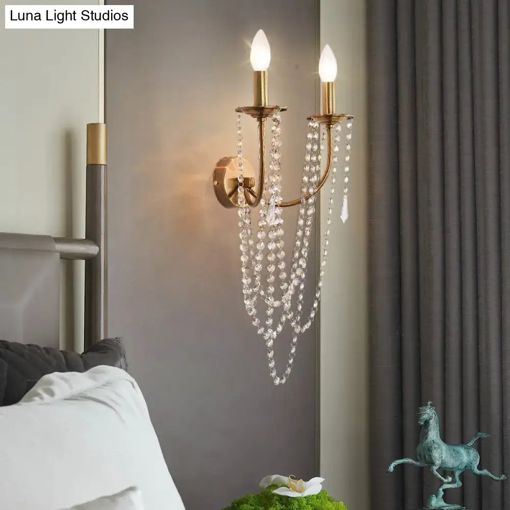 Gold-toned French country wall lamp with brushed brass finish, two lit candle bulbs, and cascading clear crystal beads