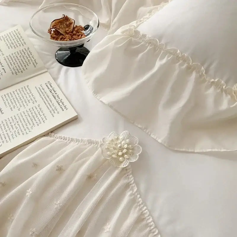 A delicate white floral brooch with pearls adorns the hem of a sheer embroidered fabric in the decorbites french princess bedding set