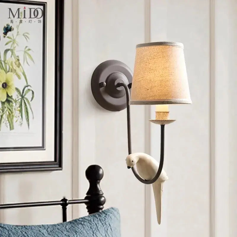 A cream ceramic bird decor antique wall lamp with a bronze arm and beige linen shade for bedroom decorbites wall lamp
