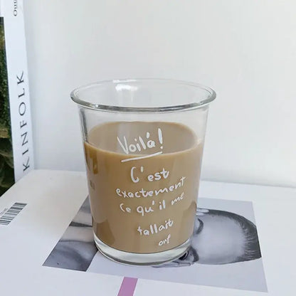 Clear glass tumbler cup with white handwritten French text filled with a light brown beverage for kitchen use