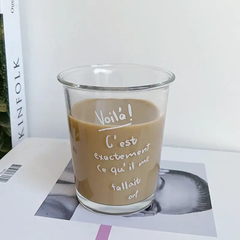 Clear glass tumbler cup with white handwritten French text filled with a light brown beverage for kitchen use