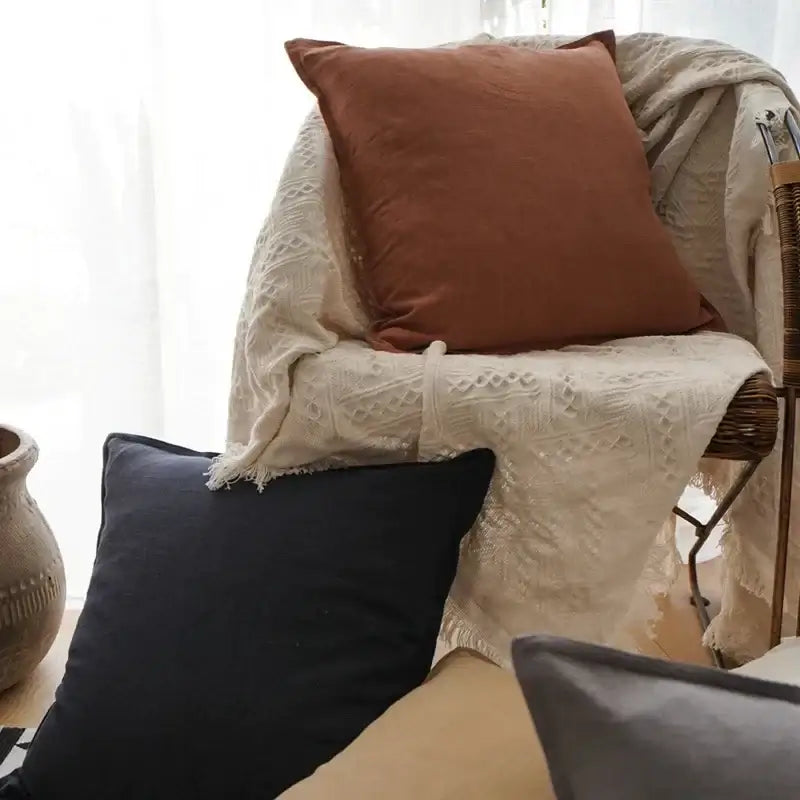 A rust-colored decorbites linen pillow with subtle texture on a woven chair with off-white lace throw for living room decor