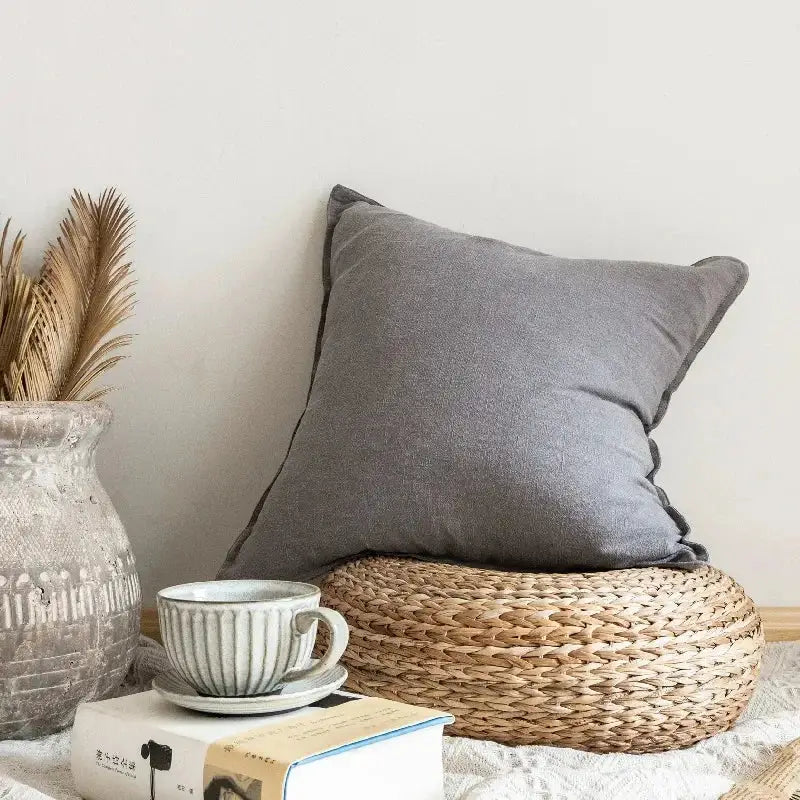 A soft gray decorbites linen pillow cover with subtle texture and neatly stitched edges on a woven wicker mat