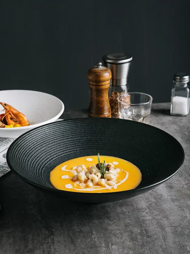 Black frosted glaze ceramic bowl with ridged texture holding orange soup garnished with rosemary from decorbites set