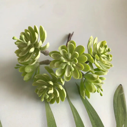 A cluster of artificial light green succulent leaves arranged on a thin stem in a frosted greenery berry stamen bundle decorbites greenery berry