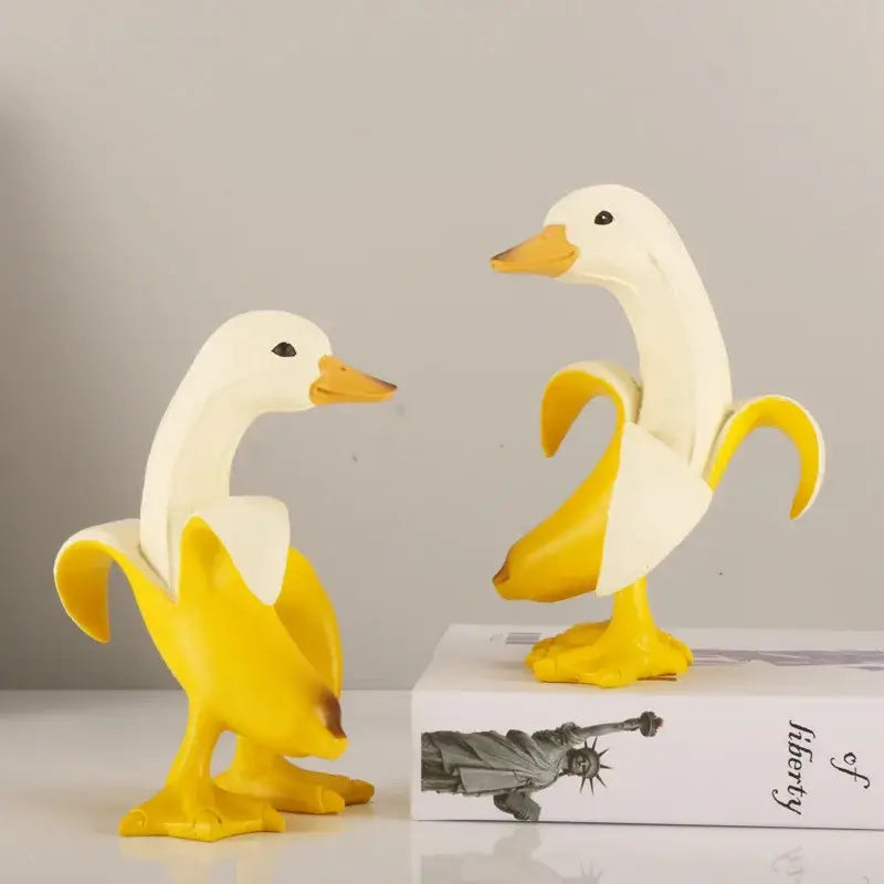 Two white duck figurines with yellow beaks and feet designed as a funny banana duck sculpture for living room decor