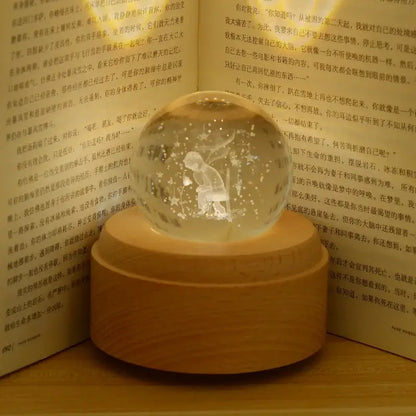 A translucent glass crystal ball music box with golden base featuring illuminated child and stars scene rotating light glow