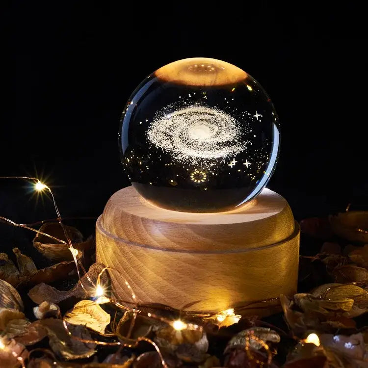 A clear crystal ball music box with detailed galaxy design resting on a light wooden rotating base for bedroom glow
