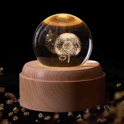 A glowing crystal ball music box with intricately etched dandelion design on a light wooden rotating base