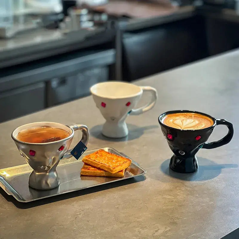 Three ceramic gemstone setting breakfast mugs in silver white and black with red gemstone accents on countertop decorbites
