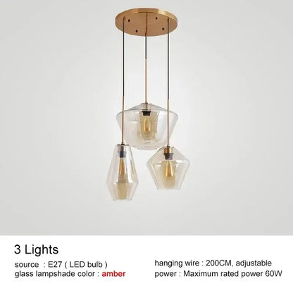 Modern brass-finished pendant light with three clear amber glass lampshades in varying geometric shapes for kitchen lighting