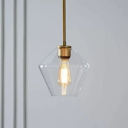 A clear glass pendant light with brass finish and exposed filament bulb from a geometric pendant lights set for living room