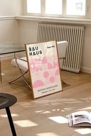 A framed decorbites™ bauhaus geometric canvas print with pink patterns and black text in a light wood frame for home decor
