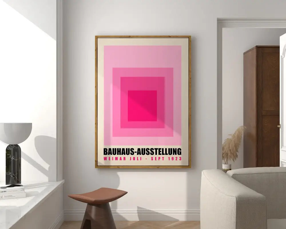 A framed bauhaus geometric canvas print with concentric pink squares and black text in a light wood frame for home decor