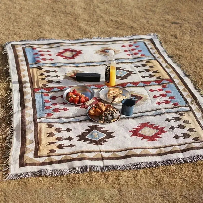 A cream-colored decorbites geometric cotton knitted sofa blanket with red blue and brown patterns and fringed edges