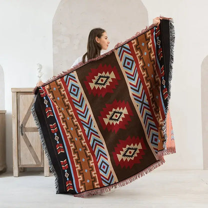 A geometric cotton knitted sofa blanket in red brown blue and beige with bold patterns and fringed edges by decorbites