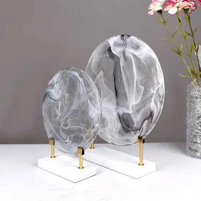 Two geometric disk marble clear glass orbs with gray and white swirls on white marble bases for home decor