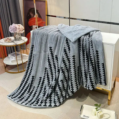 A soft light gray geometric double layer lamb fleece blanket with a black tree pattern draped over a white cabinet