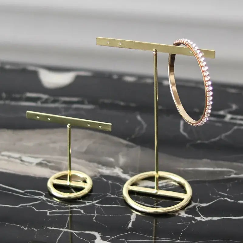 Geometric gold jewelry display rack with a gold metal stand holding a rose gold hoop bracelet with pink crystals